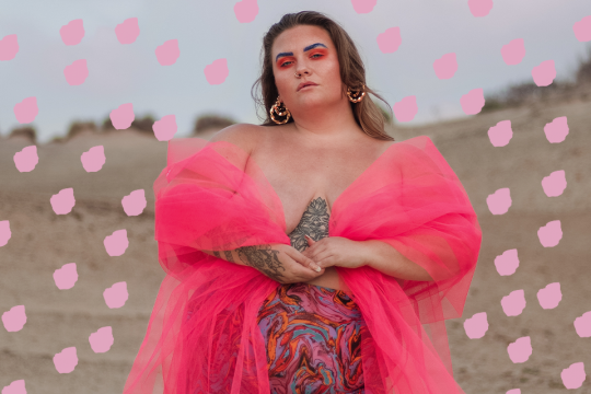 Lotte van Eijck, een prachtige curvy vrouw, staat krachtig in het midden van een zandvlakte in een roze jurk.