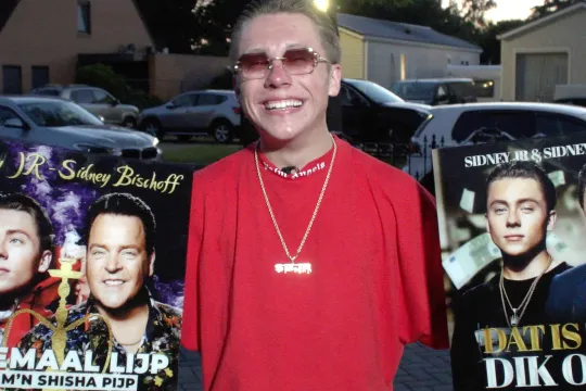 Sidney in rood shirt met twee reclameposters van zijn single