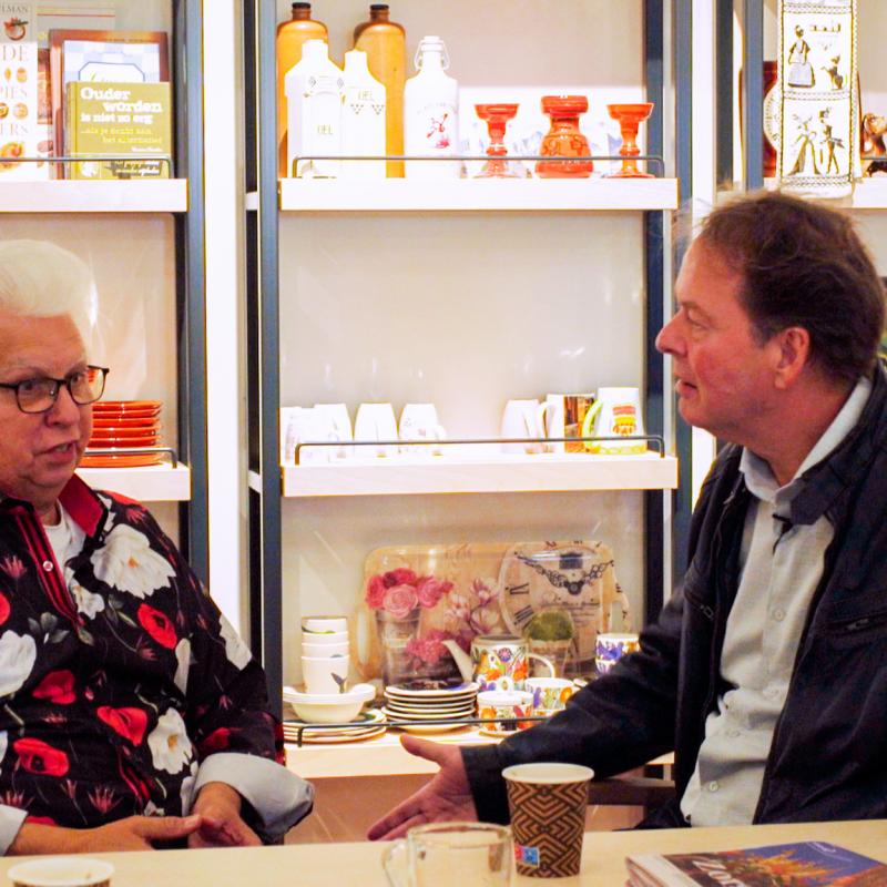 presentator Ron Kas (rechts) in gesprek met bewoner Hans (links), zittend aan tafel