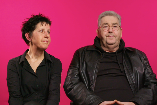 Margo en Bert voor een roze achtergrond in Burgerzaken