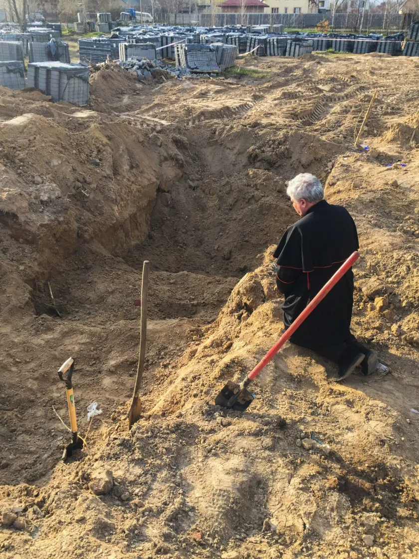 This photo handout on April 15, 2022 by Vatican Media shows Papal Almoner, Polish Cardinal Konrad Krajewski kneeling to pray by a mass grave in the grounds of the St. Andrew and Pyervozvannoho All Saints church in the Ukrainian town of Bucha, northwest of Kyiv. 