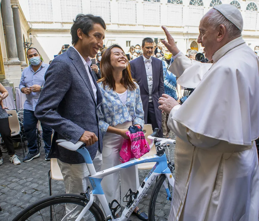 A photo taken and handout on June 16, 2021 by The Vatican Media shows Pope Francis (R) giving his blessing to Colombia's cyclist Egan Bernal (L) and his girlfriend Maria Fernanda Gutierrez, presenting the Pope Francis with an Ineos Grenadier team jersey and a bicycle, during the Pope's weekly general audience at San Damaso courtyard on June 16, 2021 in The Vatican. 
