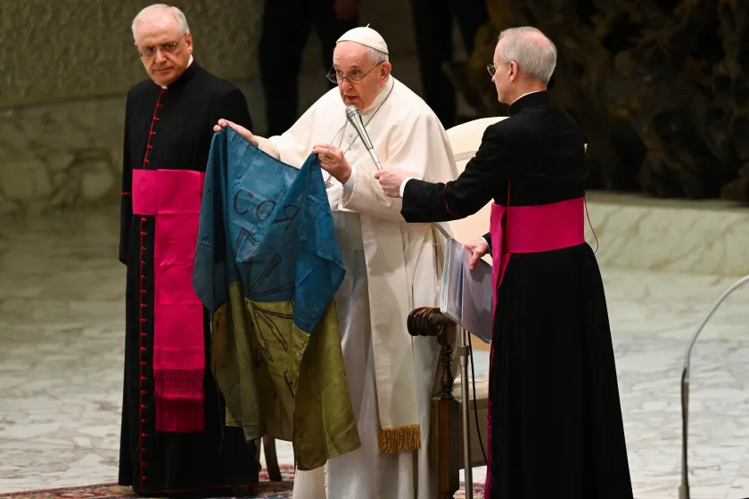 Pope Francis speaks while holding a flag of Ukraine that comes from the city of Bucha, one of the areas around Ukraine's capital from which Russian troops have withdrawn and where dozens of bodies in civilian clothing have been found, during the weekly general audience on April 6, 2022 at Paul-VI hall in The Vatican. 
