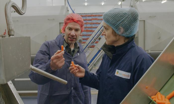 Teun van de Keuken in een fabriek met een babygroente wortel in zijn hand